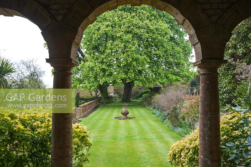 View towards magnificent horse chestnut at the end of a grassy terrace with sundial, seen framed by the arches of the Italianate loggia. Wayford Manor, Wayford, Crewkerne, Somerset, UK