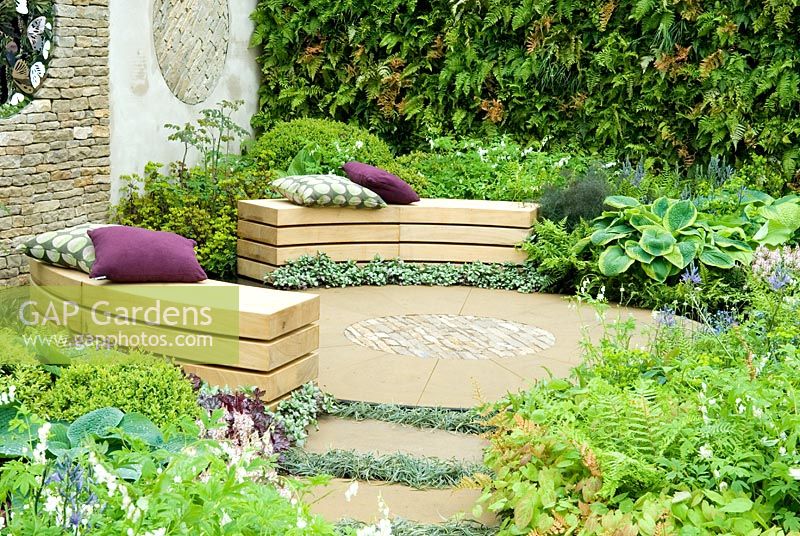 Circular seating area in a relaxing garden of lush planting, with decorative dry stone wall and fern wall providing  backdrop - 'A Place to Reflect', Gold Medal Winner - RHS Malvern Spring Show 2012