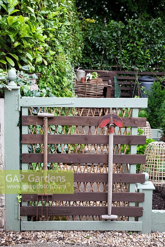 Painted wooden gate decorated with vintage garden tools, leading to vegetable garden. Garden Neighbours