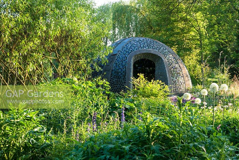 Dome structure constructed using empty bottles, with white Allium stipitatum 'Mount Everest' in foreground - Westonbury Mill
