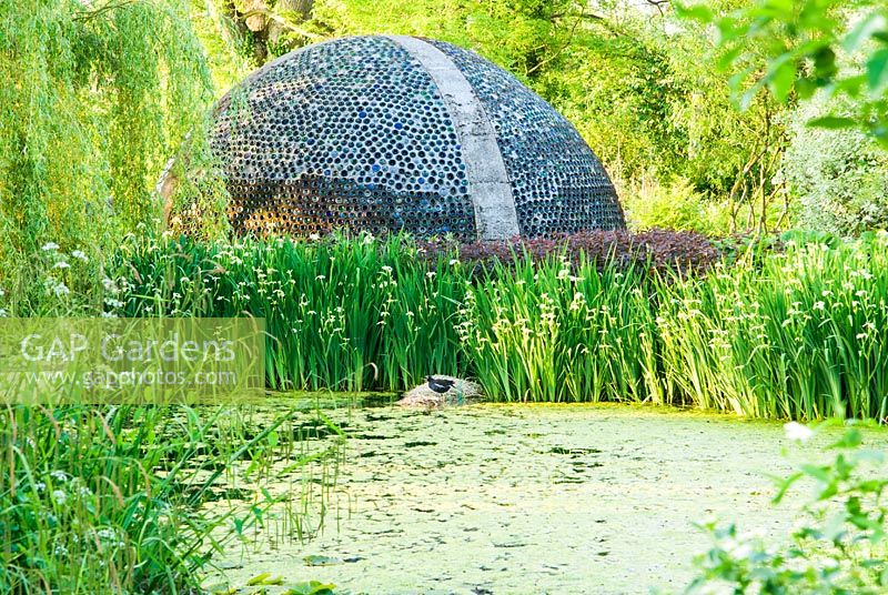 Dome structure constructed using empty bottles viewed over pond - Westonbury Mill 
 