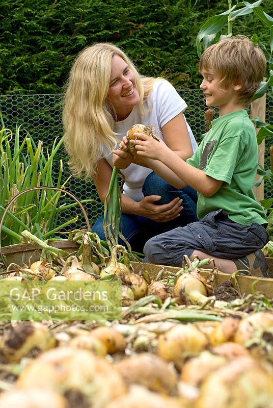 Mother with her seven year old son in vegetable garden collecting onions