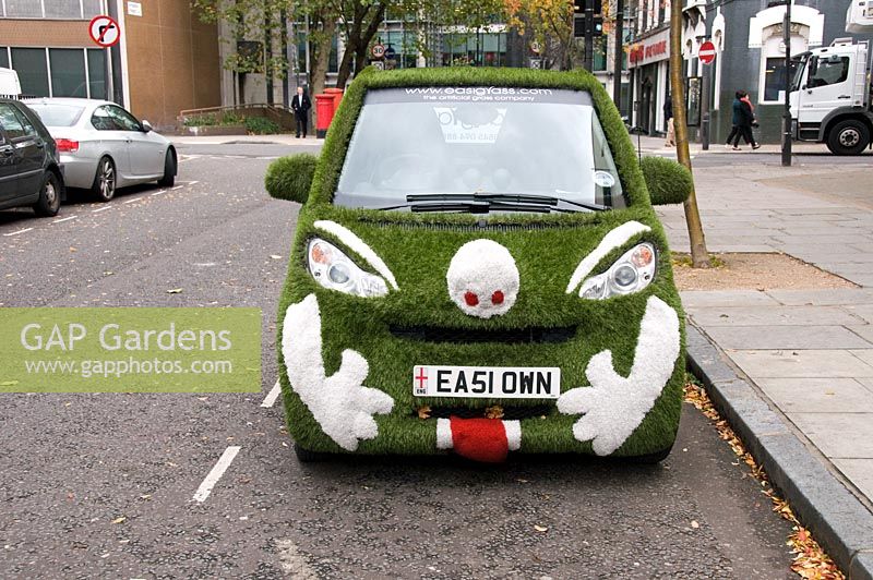 Front of car covered in artificial grass advertising the company supplying the product with a face picked out in white grass at the front, street in Marylebone, London
