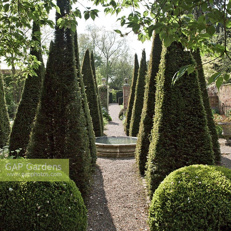 Carved limestone wellhead, Four quadrant beds separated by tall thin yew spires in a cruciform, in a country garden with an emphasis on perennials strong design 