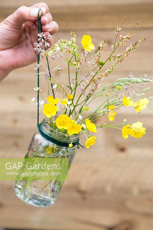 Wild buttercups and grasses arranged in glass jar vase