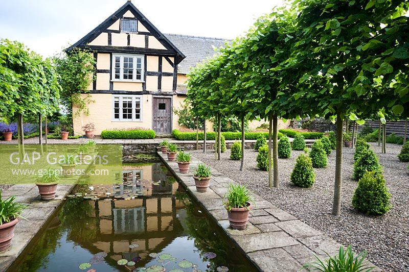 The Canal, framed by pleached limes and pots of agapanthus, with 16th century house behind. Ashley Farm, Stansbatch, Herefordshire, UK