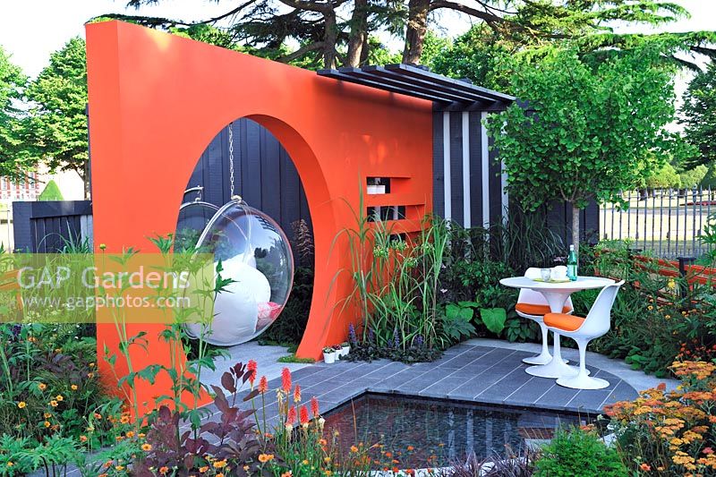 Contemporary table and chairs on patio by pond,Orange Moongate wall with hanging bubble chairs. Mid Century Modern, RHS Hampton Court Flower show 2013, Design -  Adele Ford and Susan Willmott