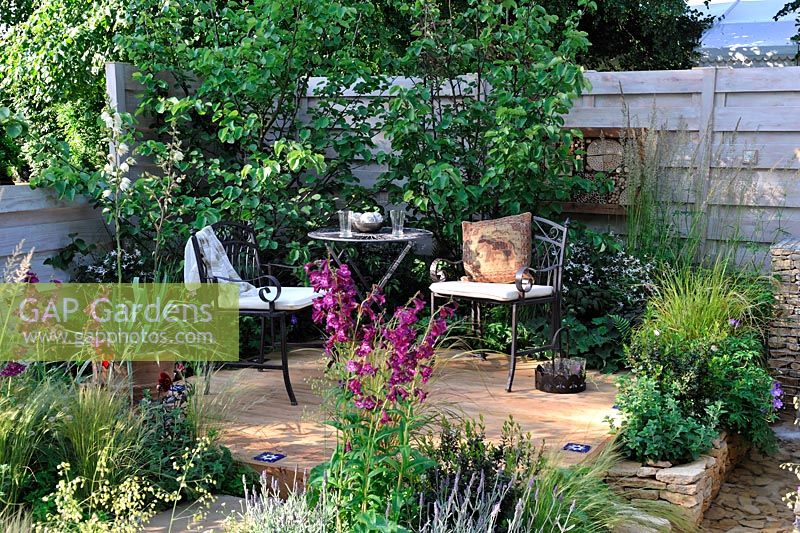 Courtyard patio. Table and chairs on decking with extensive planting in gravel beds.Penstemon Raven, Dahlia, Ergeron, salvia and grasses. Four Corners, RHS Hampton Court Flower Show 2013, Design -  Peter Reader
