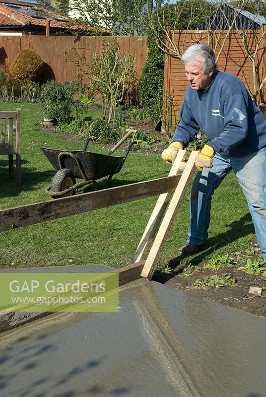 Man using home made levelling device for screeding concrete in the base of a garden DIY project