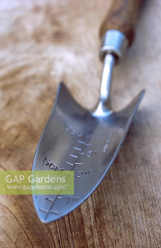Metal trowel with a measurement depth scale on a wooden surface