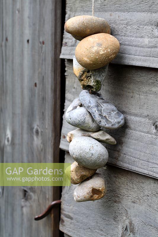 Pebbles with holes hanging from string against a wooden shed