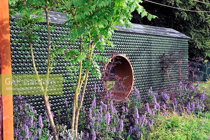 Recycled wine bottle garden wall, fitted with solar panels, Agastache foeniculum, Koelreuteria paniculata. Greenco Sense garden. RHS Tatton Park Flower Show