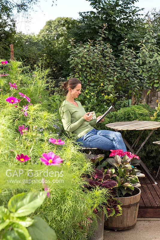 Woman reading newspaper and drinking tea in small suburban garden