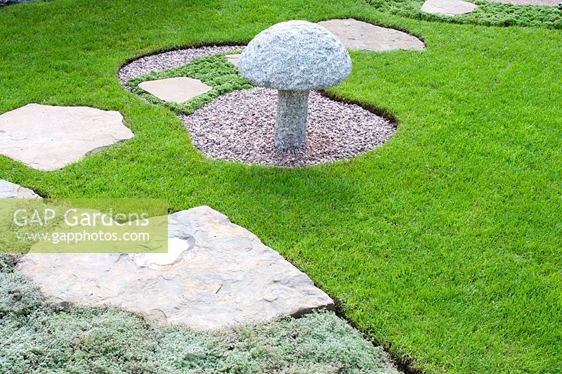 Stepping stone path across lawn and Thymus pseudolanuginosus with decorative stone mushroom in circular gravel bed in 'Reflections of Japan'. Gold medal winner at RHS Tatton Flower Show 2013