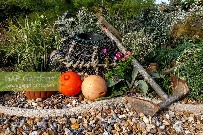 Coastal themed bed with gravel, lobster pot and rope as border. Driftwood garden
