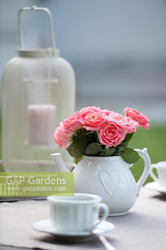 Bouquet of pink roses in teapot with heart design and shabby chic openwork lantern on the table