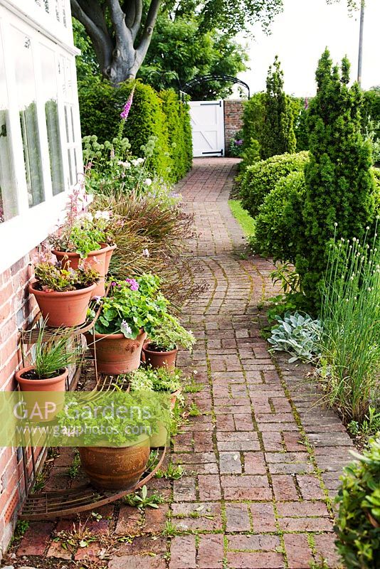 Decorative brick path with structural conifers and decorative etagere with containers 