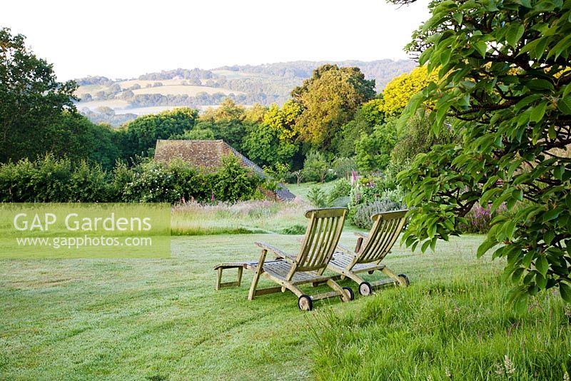 Wooden deckchairs on lawn overlooking summer borders and Sussex countryside