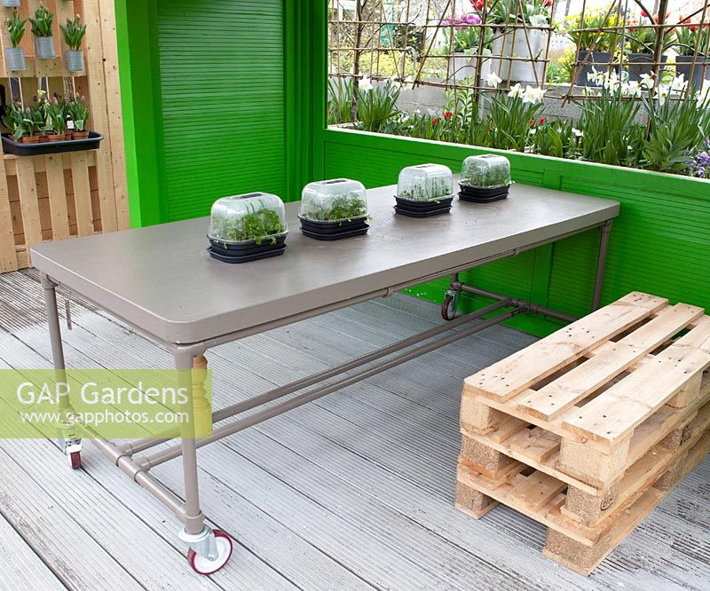 Miniature greenhouses with herbs on industrial table in the green cabin with stacked pallets used as a seat.
