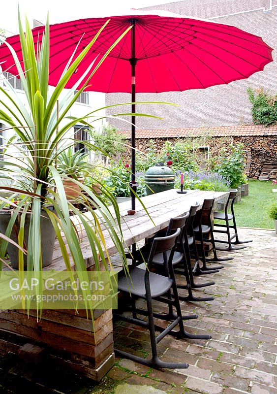 Red japanese umbrella with long table made of recycled wooden boards. Black rocking chairs from Ikea.