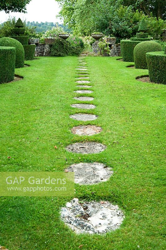 Circular stone paving slabs form a path across the lawn of the Topiary Garden