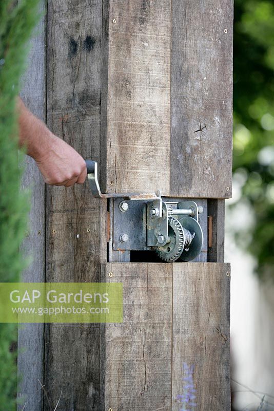 Hand using mechanical device for closing wooden screen at back of garden. 'A Room with a View'. RHS Hampton Court Flower Show 2013.  