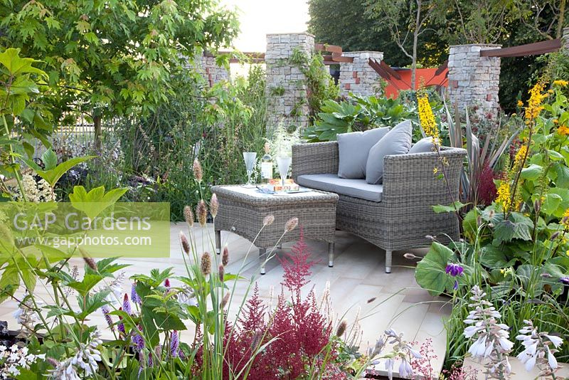 Seating on terrace with planting of  Astilbe, Hosta, Ligularia and Primula vialii