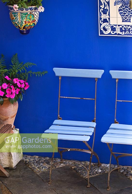 Small town garden - Courtyard with cobalt blue walls, blue cafe chairs and ceramic picture from Portugal, ceramic container and terracotta pot.