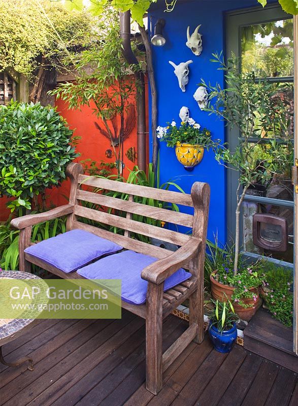 Decked area with colourfully painted feature walls and seating area.  Small town garden, Brighton, UK 