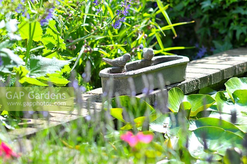 Bird bath with birds sculptures on the stone border of the garden pond.