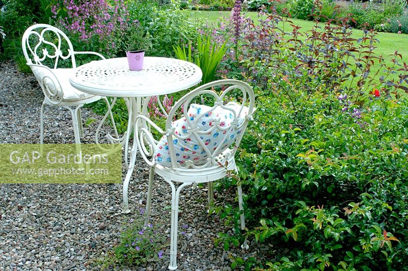Ornamental white metal table and chairs on gravelled area of cottage garden 