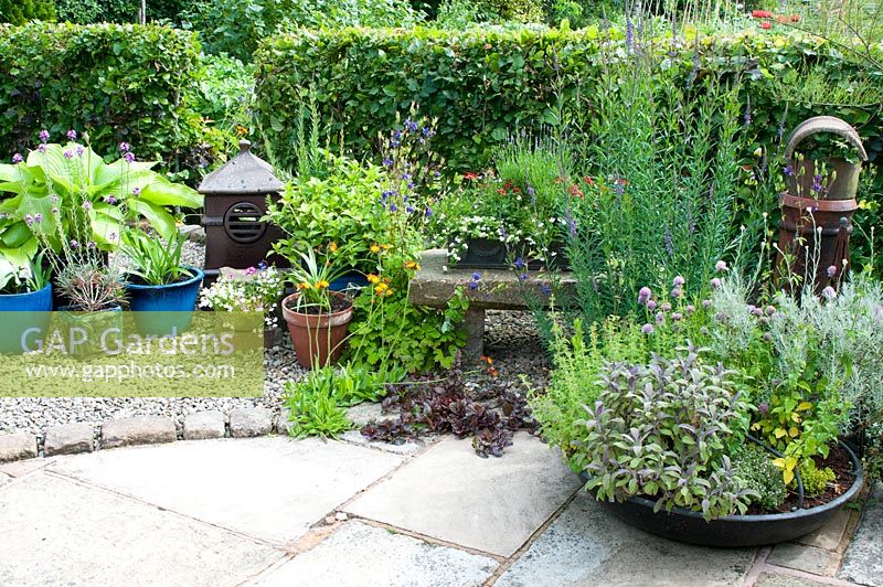 Stone patio and gravelled area with arrangement of containers and plants 