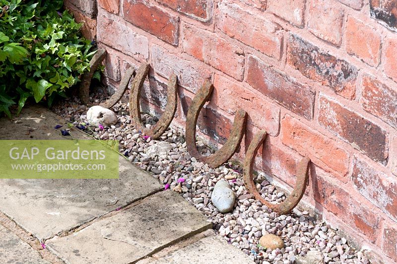 Old horseshoes against red brick wall by stone path
