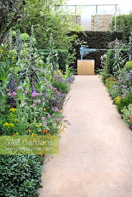 Flowering borders including Echium pininana, Geranium maderense and Geum with pathways and sculpture in The Lucid Garden in The Arthritis Research UK Garden