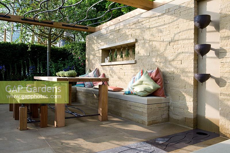 Outdoor taverna style eating area with stone wall, table, chairs and wall mounted water feature