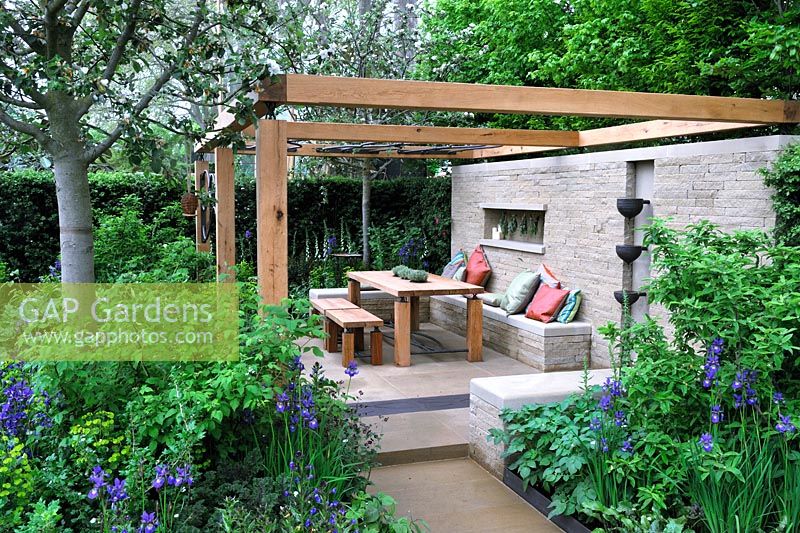 Outdoor seating and dining area with open pergola, wooden table and chairs with wall mounted water feature 