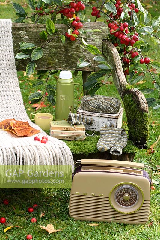A rustic, moss covered bench with thermos flask, lunchbox, woollen throw, sock knitting, Bush radio and Observer books