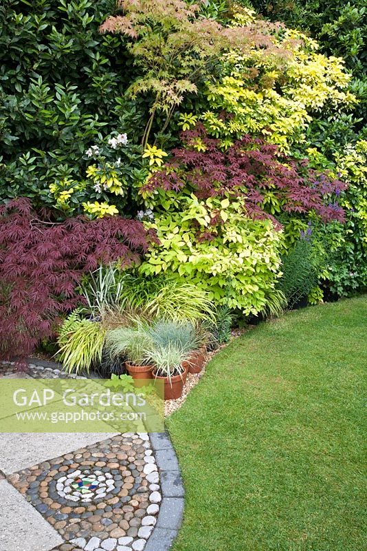 Mosaic effect stonework on patio and mixed colourful foliage of Acer and grasses in containers