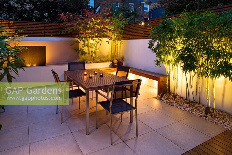 Minimalist Garden lit up at night - Acer Aconitfolium, table and chairs and Phyllostachys Aurea and water feature 