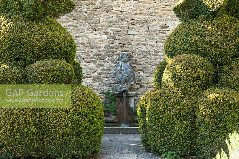 Clipped yews frame the Blue Pool, a small formal pool, with a Romanesque bas relief set into the wall above of a woman riding a lion. 