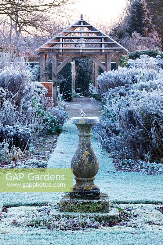 Winter garden in frost -  view to pergola with frosted lawn and borders and stone sundial at dawn. Wollerton Old Hall, Shropshire