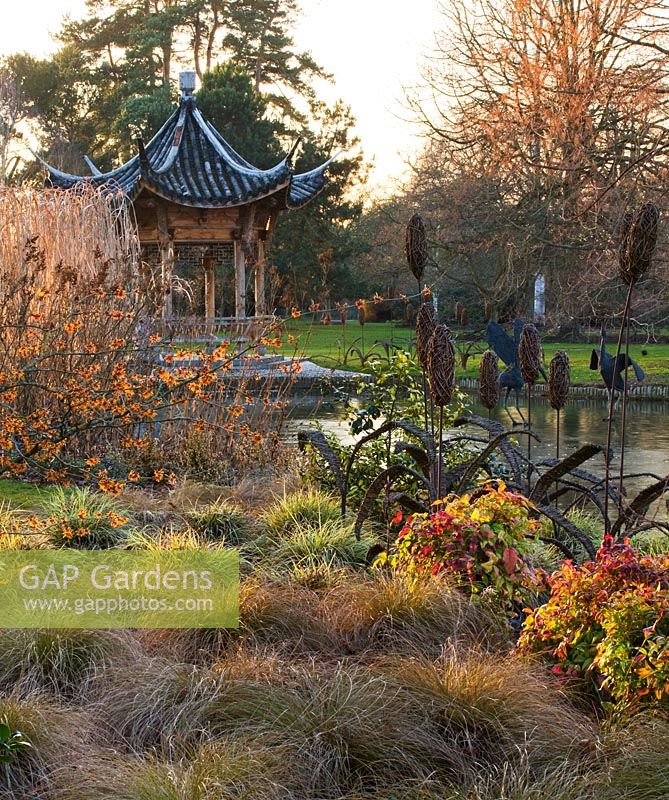 Evening view across the lake to the Chinese pagoda with Hamamelis 'Aphrodite', Carex flagellifera and Carex ashimensis 'Evergold'