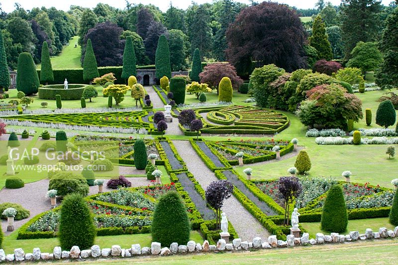 Looking over the balustrade at the stunning grand parterre garden with Buxus edged beds shaped like great fans or triangles and the whole garden studded with shaped colourful trees and topiary intermingled with statues 
