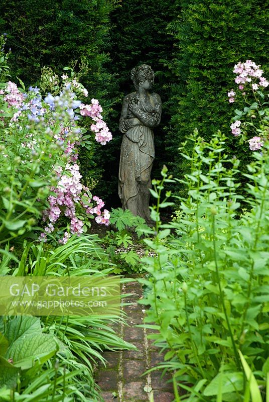Stone statue of a girl, maiden in the niche of  a Taxus - yew hedge. Rosa 'Ballerina'  Suffolk by brick path. July