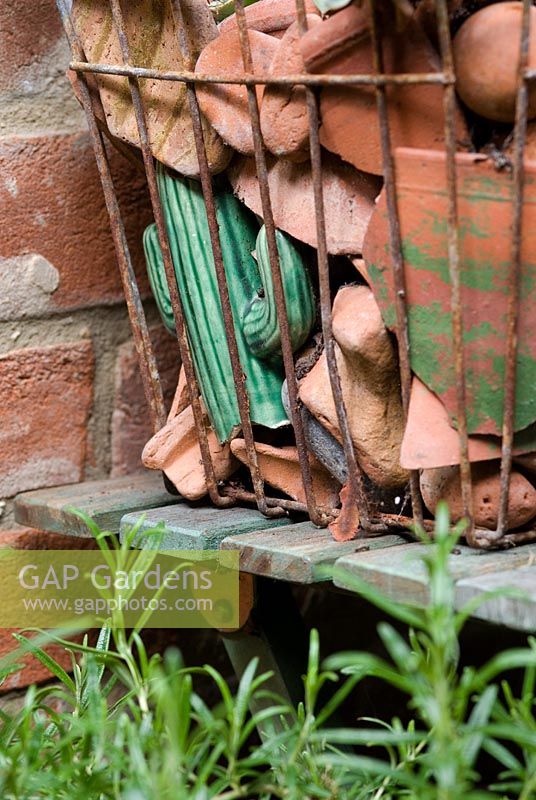 An old wire shopping basket with broken terracotta in a small town garden