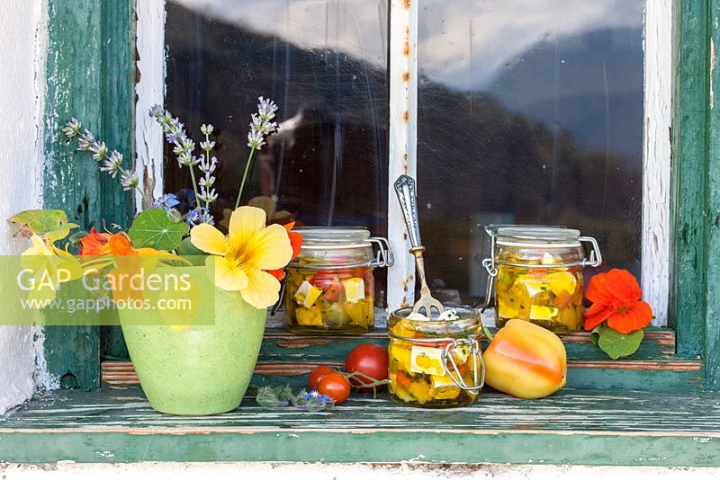 On an antique wooden window sill, glass jars with goat cheese, tomatoes, peppers and a ceramic vase with Indian cress and lavender.  Lavandula and Tropaeolum