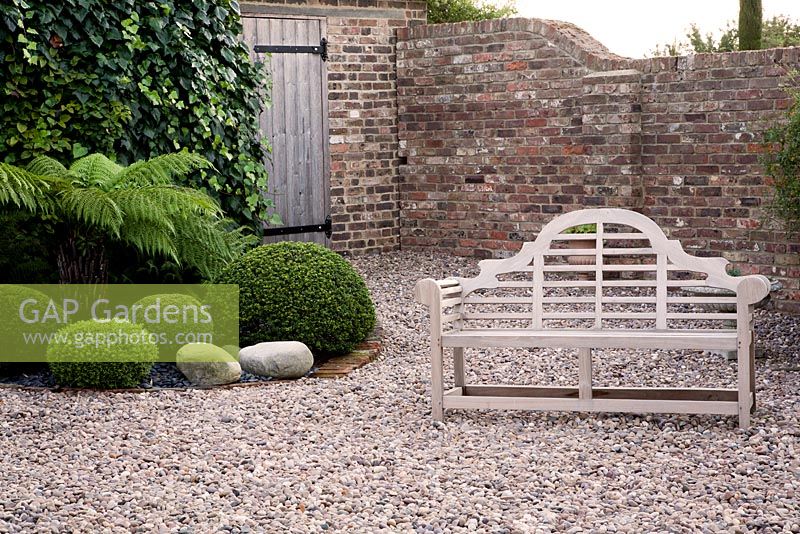 Formal gravel garden with clipped shrubs, decorative stones, Ferns and wooden seat