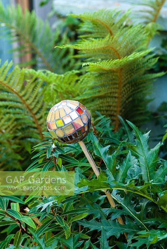 Mosaic ball on stick, designed by Anne Cardwell, in the border with ferns and Acanthus leaves in town garden