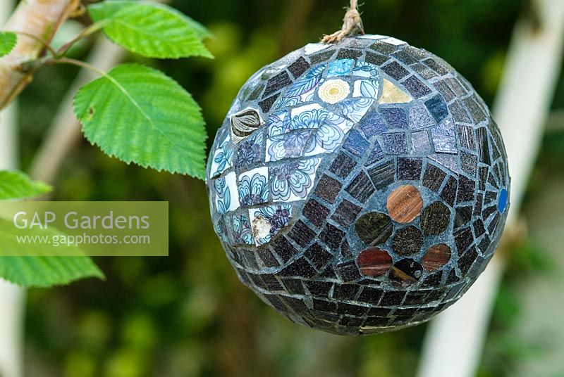 Mosaic ball, designed by Anne Cardwell, hanging from a Betula - silver birch tree in town garden