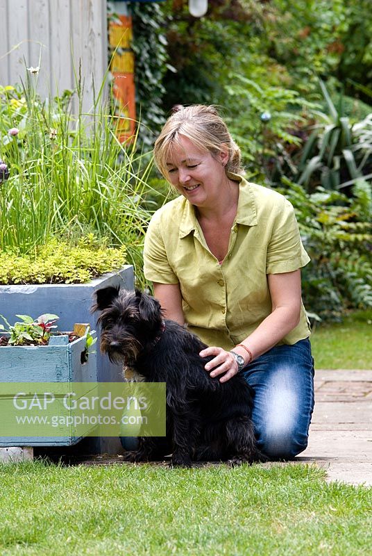 Helen Riches with her dog next to blue painted plant containers in her town garden, June